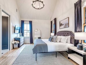 A modern bedroom with a large bed, a bedside table, a lamp, and a window with curtains. - Six-Seater Golf Cart Included! (Carlton Landing)