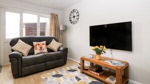 A living room with a sofa, a coffee table, a TV, and a clock on the wall.