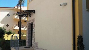 A building with a stone facade, a metal staircase, and a small garden area. - PLAYA DEL SOL Three-room apartment 1 (Santa Domenica)