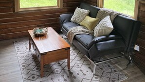 Ein gemütliches Blockhaus-Interieur mit Ledersofa, Holztisch und einem gemusterten Teppich.