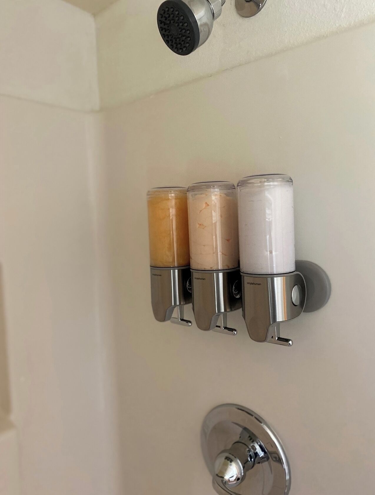 A bathroom with a showerhead, three soap dispensers, and a toilet.