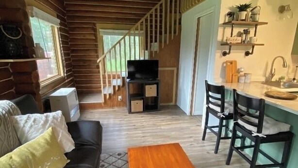 Ein gemütliches Blockhausschlafzimmer mit einer Holztreppe, einem Wohnbereich mit Sofa und Couchtisch sowie einer Küchenzeile mit Spüle und Regalen.