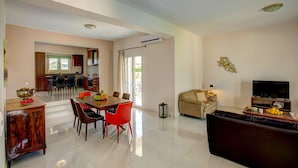 Uma sala de estar ampla com uma mesa de jantar, cadeiras vermelhas, um sofá e uma televisão.