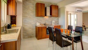 Cozinha moderna com armários de madeira, painel de pedra e área de refeições com mesa e cadeiras de vidro.