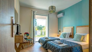 Quarto de hotel com duas camas, uma escrivaninha, uma cadeira e varanda com vista.