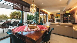A spacious living area with a dining table, sofas, and a large window overlooking a pool. - Villa Tiare 2 by Villa Plus (Ionian Islands)