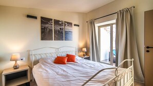 Ein Schlafzimmer mit einem Bett, zwei Nachttischen, einer Lampe, einem Fenster mit Vorhängen und drei Wandbildern.