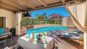 Ein überdachter Außenbereich mit Pool, Liegestühlen und einem Tisch für das Essen.