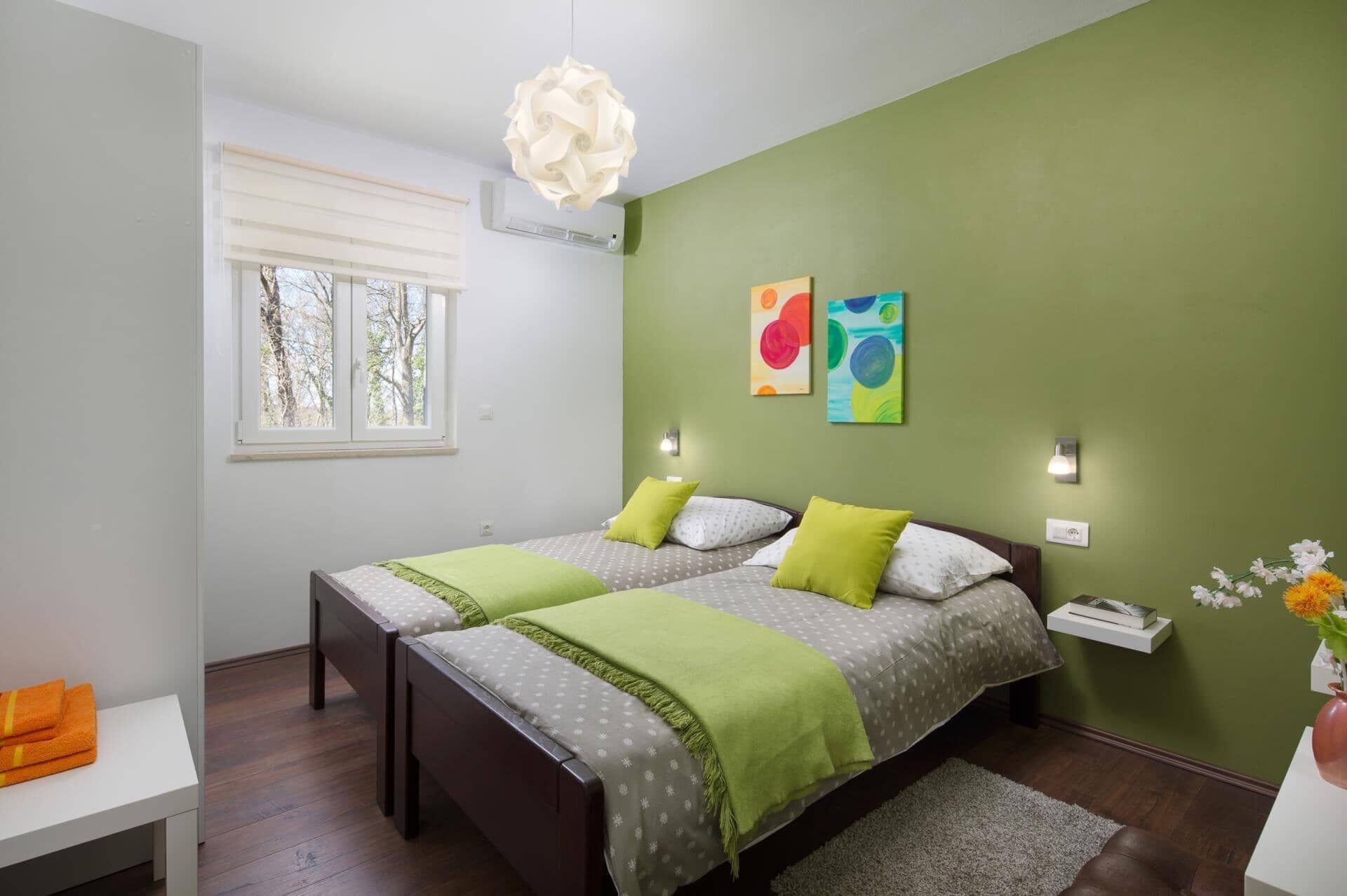 Een slaapkamer met twee bedden, een raam met zonwering, een hanglamp en kunst aan de muur.