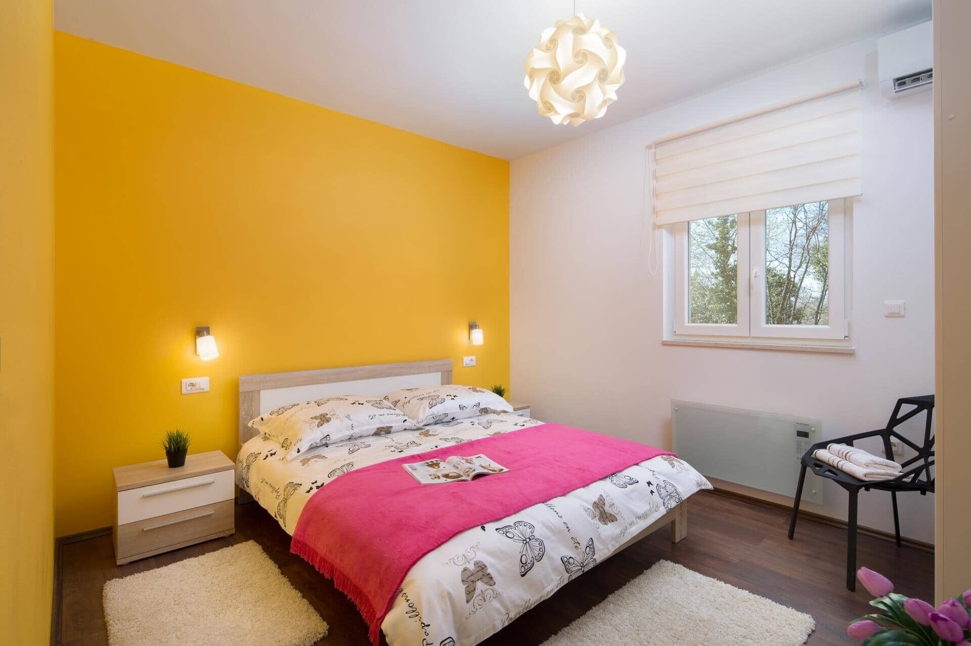 A bedroom with a bed, bedside tables, a chair, a window, and a radiator.