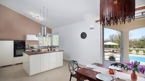 Une cuisine moderne dotée d’un îlot central, d’un coin repas avec une table dressée pour deux personnes et d’une vue sur une piscine.