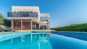 Una casa moderna de dos pisos con piscina, mobiliario exterior y un cielo azul claro.