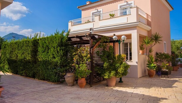 Una casa de dos pisos con balcón, plantas en macetas y una pérgola.