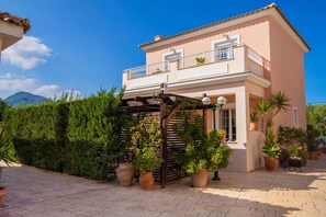 Une maison à deux étages dotée d’un balcon, de plantes en pot et d’une pergola.