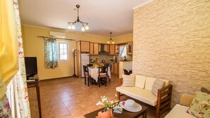 Una sala de estar acogedora con un sofá, una mesa de centro con un sombrero y flores, una zona de comedor con una mesa y sillas, y una cocina con armarios de madera y una estufa.