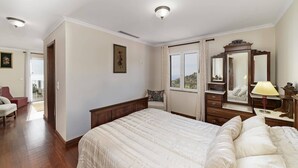 Un dormitorio con una cama grande, un tocador con espejo, una ventana con vistas y una puerta que da a otra habitación.