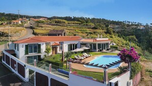 Una villa moderna con piscina, varios balcones y vistas a las colinas circundantes.