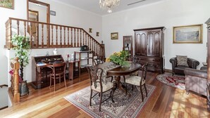 Un amplio salón con una escalera de madera, una mesa de comedor con sillas, un gran aparador de madera y un candelabro.