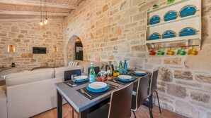 A stone-walled dining area with a table set for four, a sofa, and a TV mounted on the wall. - Villa Rizolia Enea by Villa Plus (Koridallos)