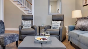 A living room with two grey armchairs, a grey sofa, a coffee table with a tray of snacks and glasses, a staircase in the background, and a mirror on the wall. - The Sterling- walk to everything Luray has to offer! Chef available (Luray)