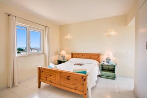 Quarto com cama de madeira, duas mesas de cabeceira com luminárias, janela com cortinas e vista para o exterior.