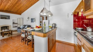 Een gezellige woonkamer met een open haard, een eethoek met een tafel en stoelen, een keuken met rode tegels, en een houten plafond.