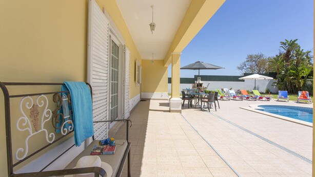 A poolside area with a covered seating area, a table with chairs, and a pool with a geometric tile pattern.