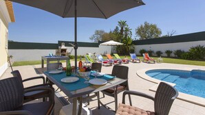 An outdoor pool area with lounge chairs, a barbecue grill, and a dining table set for a meal.
