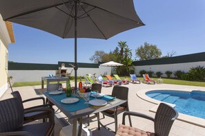 An outdoor pool area with lounge chairs, a barbecue grill, and a dining table set for a meal.