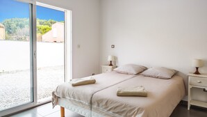 A bedroom with a large sliding glass door leading to an outdoor area, a bed with two pillows and a blanket, and bedside tables with lamps. - Villa Terre Des Vins by Villa Plus (Portel-des-Corbières)