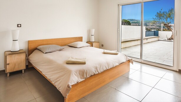 A bedroom with a wooden bed, two bedside tables, and a large sliding glass door leading to an outdoor terrace. - Villa Terre Des Vins by Villa Plus (Portel-des-Corbières)