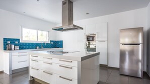 A modern kitchen with white cabinetry, a stainless steel refrigerator, and a blue-tiled backsplash. - Villa Terre Des Vins by Villa Plus (Portel-des-Corbières)
