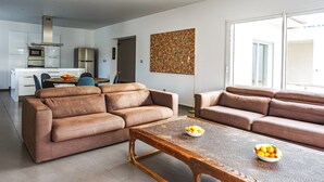 A modern living room with two sofas, a coffee table with fruit, and a kitchen in the background. - Villa Terre Des Vins by Villa Plus (Portel-des-Corbières)