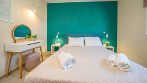 Een hotelkamer met een muur in teal, een bed met witte beddengoed, een bureau met spiegel, en twee bedlampjes.