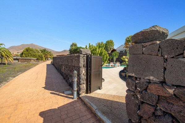 Ein Weg führt zu einem Poolbereich mit einer Steinmauer, einem Metalltor und einem Berg im Hintergrund.