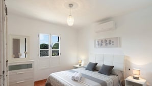 Une chambre à coucher avec un lit, des tables de chevet, un miroir, une fenêtre et un luminaire au plafond.