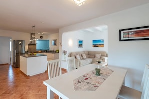 Een moderne keuken met een centraal eiland, een eethoek met een tafel, en een woonkamer met een bank.