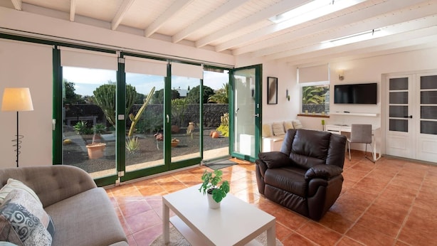 Un vaste espace de vie avec une porte-fenêtre coulissante donnant sur un jardin, un canapé en cuir, une table basse et un téléviseur à écran plat fixé au mur.