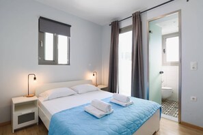 A bedroom with a bed, bedside tables, a window with curtains, and a bathroom visible through an open door.