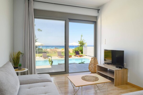 A modern living room with a large sliding glass door leading to a poolside area, a flat-screen TV, and a comfortable sofa.