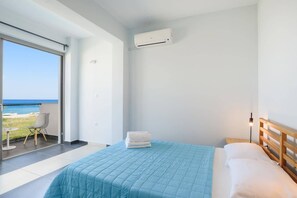 A bedroom with a bed, a wooden headboard, a window with a view of the beach, and an air conditioning unit.