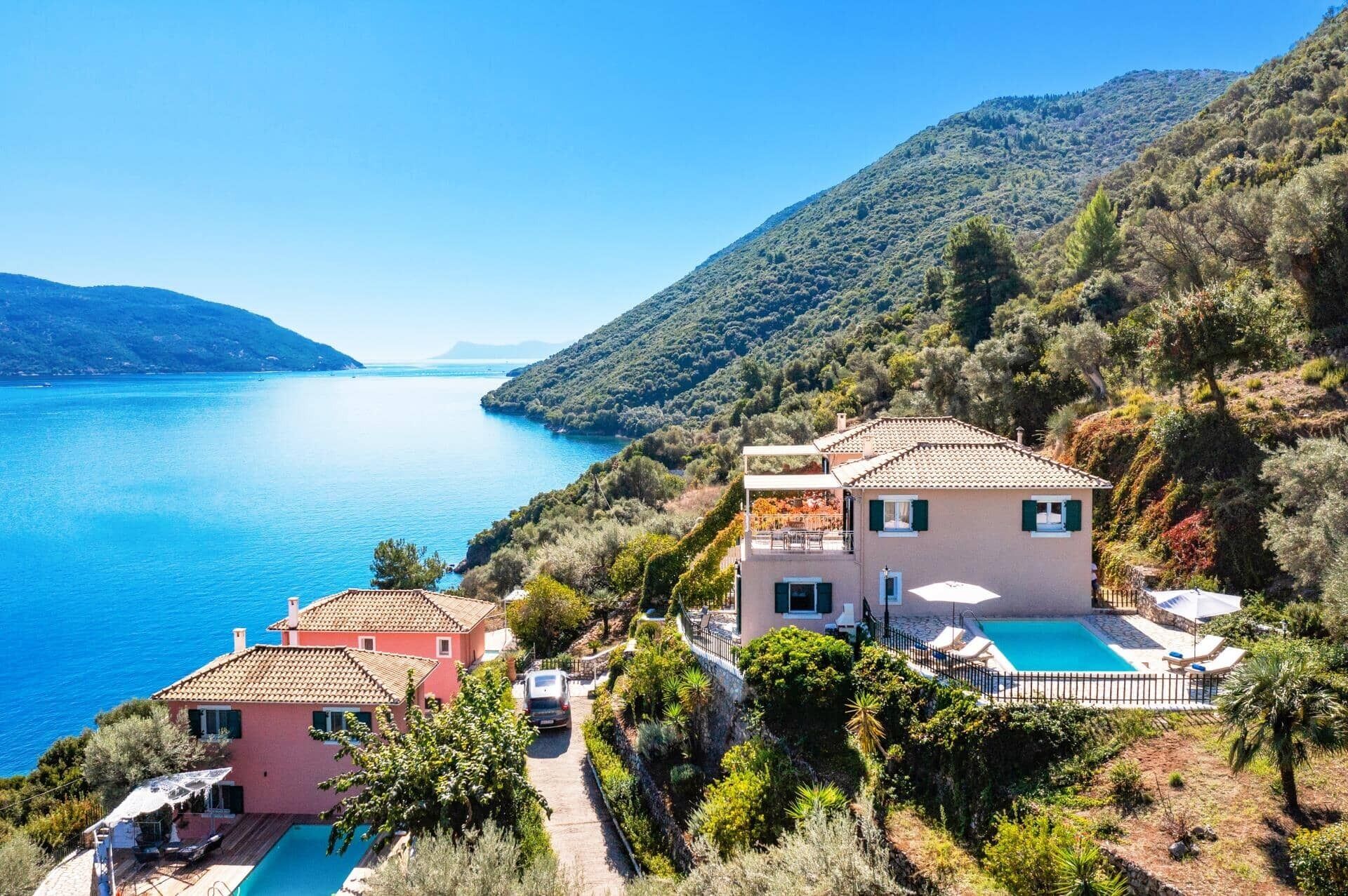 Une propriété située sur la côte, dotée d’une piscine, d’une maison rose et d’un bâtiment plus grand avec un balcon.