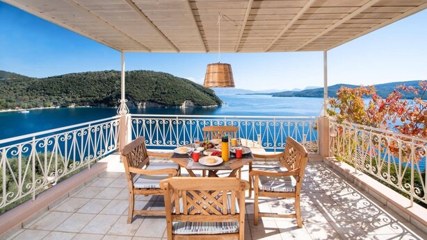Une terrasse avec une table dressée pour deux personnes, offrant une vue sur la côte et un ciel dégagé.
