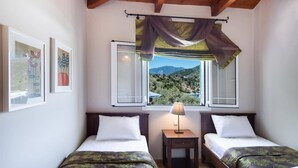 A bedroom with two beds, a nightstand, a lamp, and a window with a view of a mountainous landscape. - Villa Floisvos Desimi by Villa Plus (Lefkada)