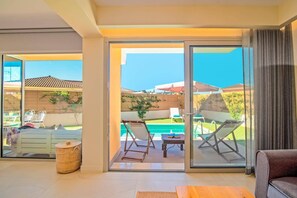 Uma sala de estar moderna com uma porta de vidro que dá para um pátio com piscina, móveis de exterior e vista para a paisagem circundante.