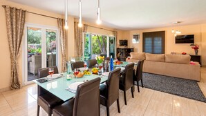 A dining area with a glass table, chairs, and a buffet setup. There is a sofa and a television in the living area. - Villa Paraisos Sol by Villa Plus (Las Lagunas de Mijas)