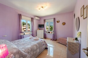 Ein Schlafzimmer mit einem Bett, einem Schminktisch, einem Fernseher und einem Fenster mit Blick auf Palmen.