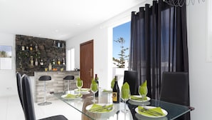 A modern dining area with a glass table, black chairs, and a stone wall backdrop. - Villa Sunny Side by Villa Plus (Puerto del Carmen)
