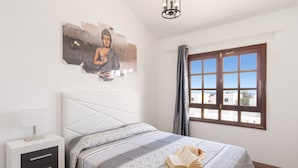 A bedroom with a bed, a bedside table, a window, and a wall art piece. - Villa Sunny Side by Villa Plus (Puerto del Carmen)