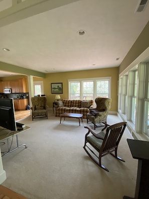 A living room with a sofa, chairs, a coffee table, and a TV. There is a kitchen in the background. - Solar-eV Country Home - Quaint Cazenovia! (Cazenovia)